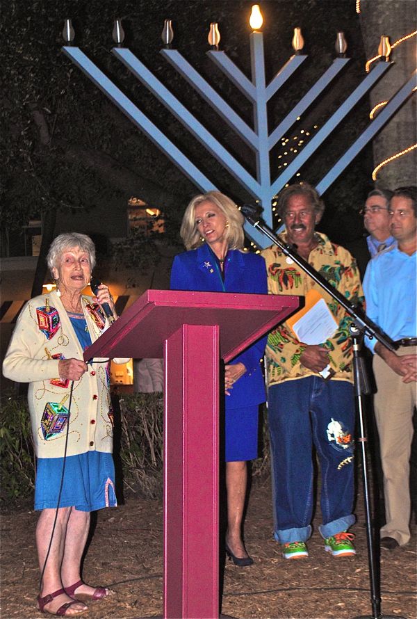 Kings Point resident Irene Wolins, left, sings a traditional Jewish prayer to mark the lighting ceremony. Andre Fladell, who donated the menorah to the city, stands between Sen. Maria Sachs and Vice Mayor Adam Frankel. 